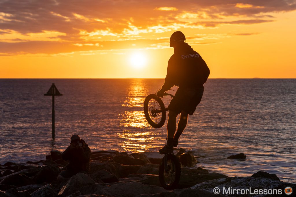 silhouette of a professional mountain biker doing figures in front of the sea at sunset time