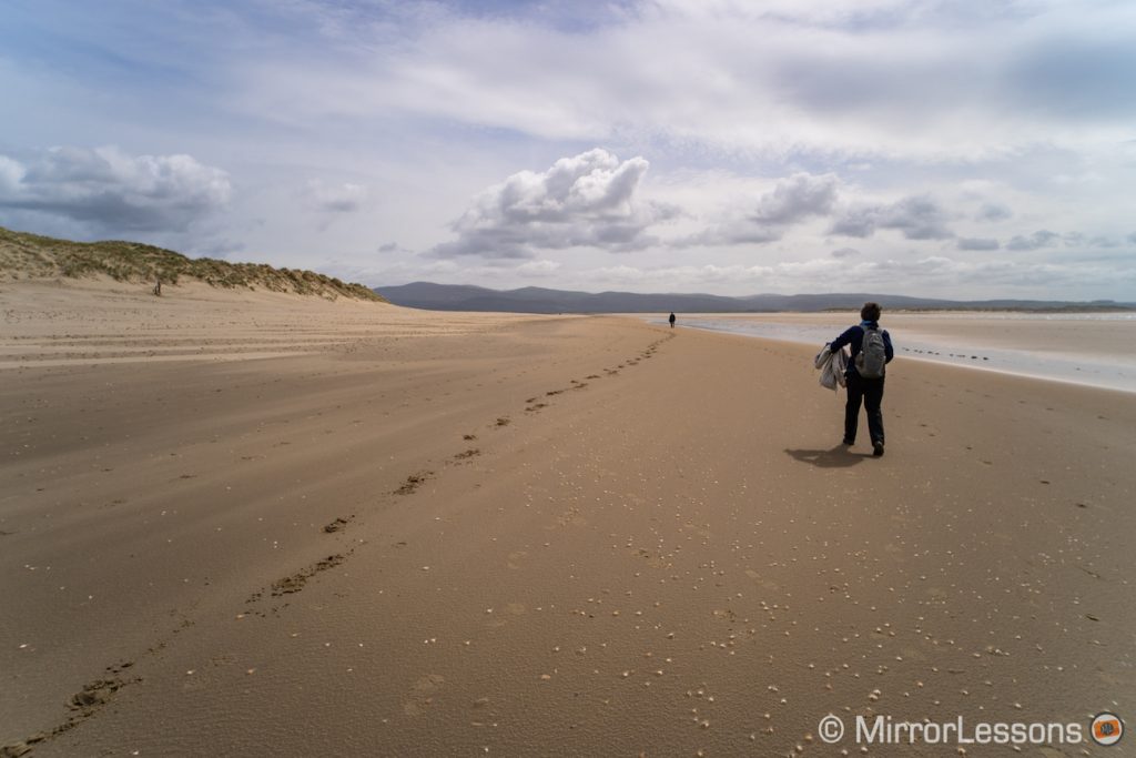 woman in the distance on the right walking on the beach, and trail of footsteps on the left