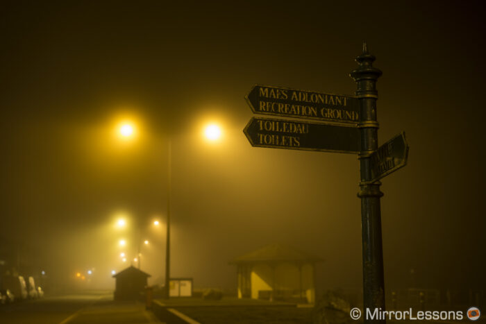 sign with directions at night with street light and fog in the background