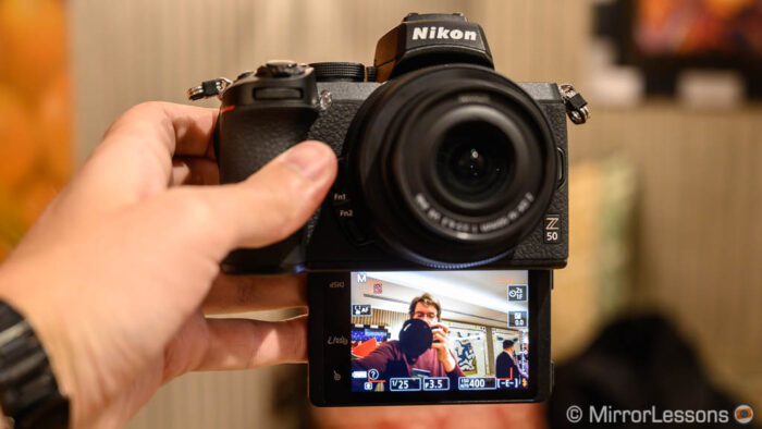 Hand holding the Nikon Z50 with 16-50mm lens and LCD screen tilted down 180˚ (selfie mode)