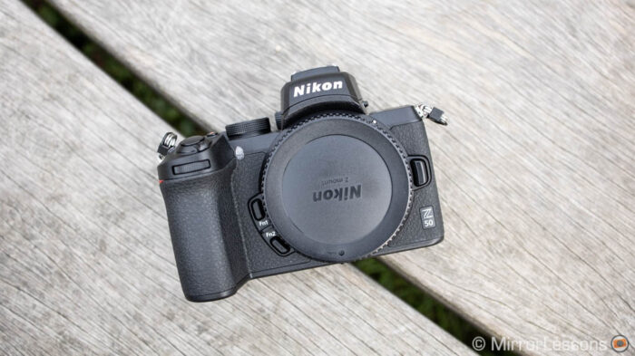 nikon z50, front view, on a wooden bench, with no lens but with sensor cap on.
