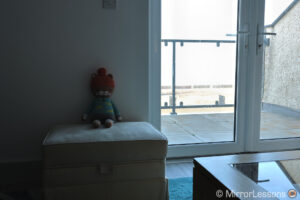Sala de estar con ventana a la derecha que muestra un balcón al aire libre y el mar de fondo