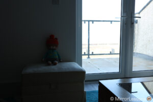 Sala de estar con ventana a la derecha que muestra un balcón al aire libre y el mar de fondo