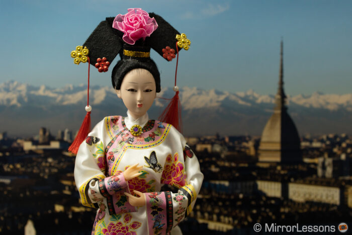 Japanese doll in front of the photo of a city panorama in the background. The image is darker than the next one.