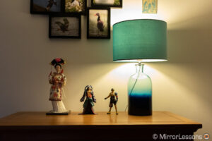 una muñeca japonesa y dos figuras de acción de final fantasy junto a una lámpara, en una cómoda.  La imagen está correctamente expuesta.