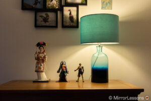 una muñeca japonesa y dos figuras de acción de final fantasy junto a una lámpara, en una cómoda.  La imagen está correctamente expuesta y tiene más detalles en las áreas brillantes.