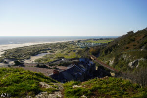 Vista desde la cima de la colina de la costa con un sitio de caravanas lejano, pastos verdes, casas y una vía férrea