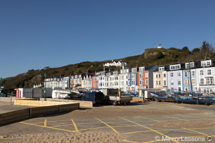coloured houses of a costal town with the hill in the background and a parking lot in the foreground