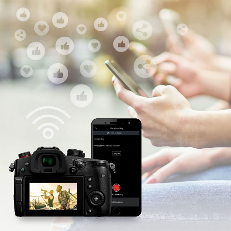 photo editing showing the rear of the GH5 II, the Lumix Sync app on a smartphone and hands in the background holding the phone