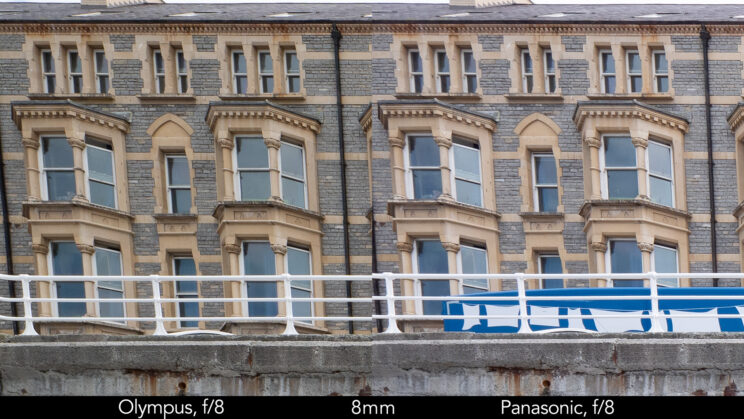 side by side enlargement of top left corner (details of the buildings) showcasing the quality at 8mm and f8 for the two lenses