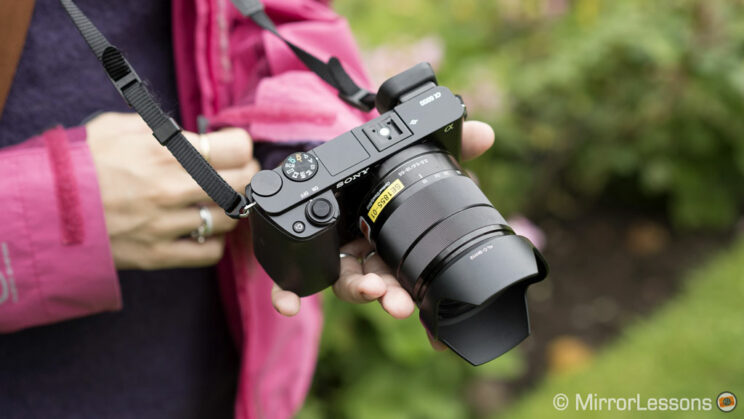 female hand holding the A6000 with 18-55mm attached, showing the top part of the camera