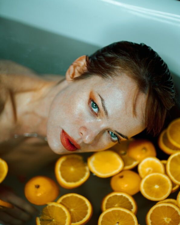 head shot of a woman lying in the bath tub with orange slices in the water