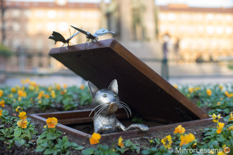 urban art installation featuring a metal cat coming out of a manhole