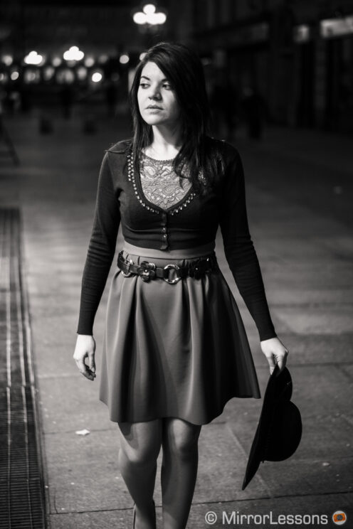 young woman walking in the street at night, holding a dark hat in her hand, black and white image