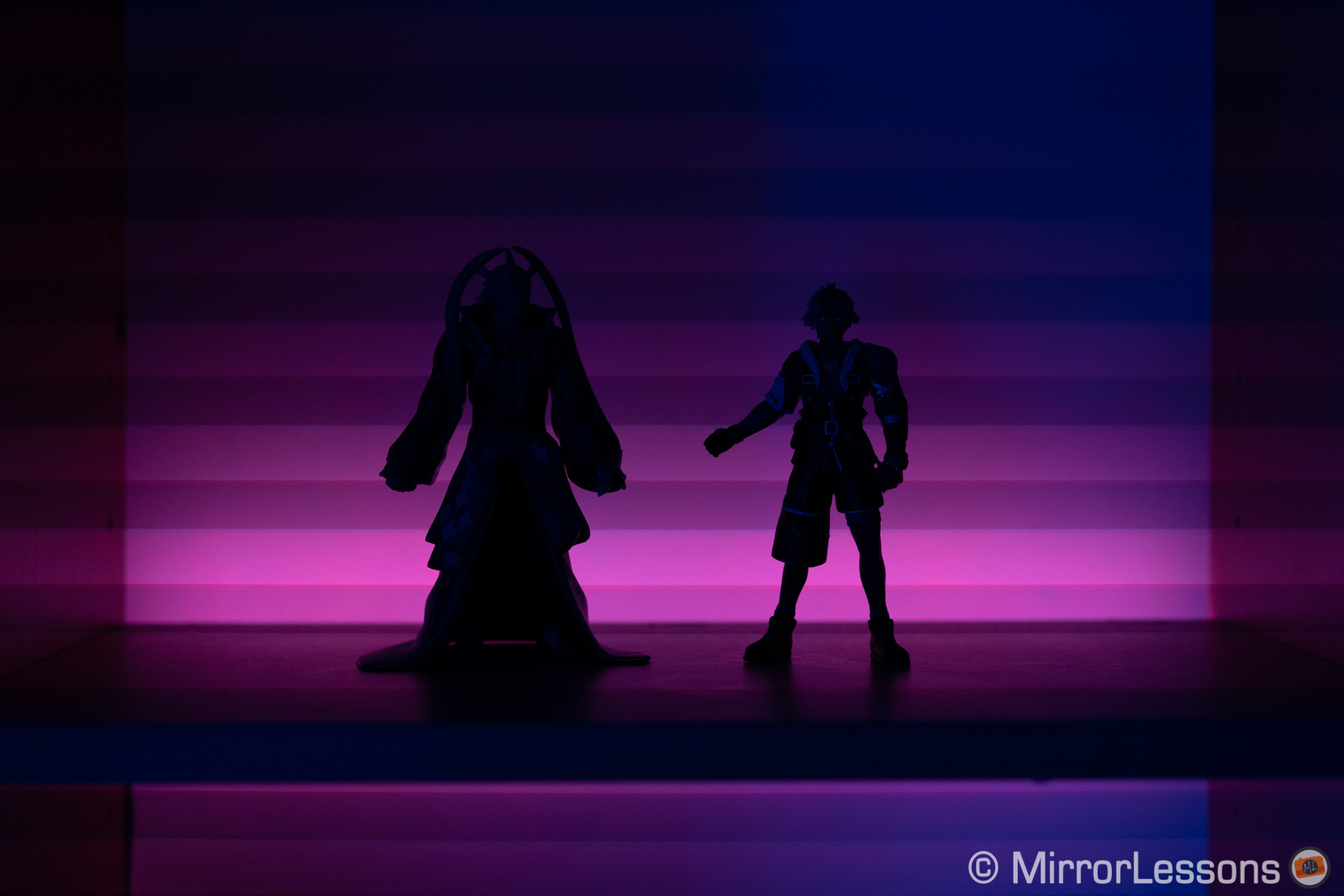 Silhueta de duas figuras de ação, com luz LED roxa ao fundo. Faixas visíveis