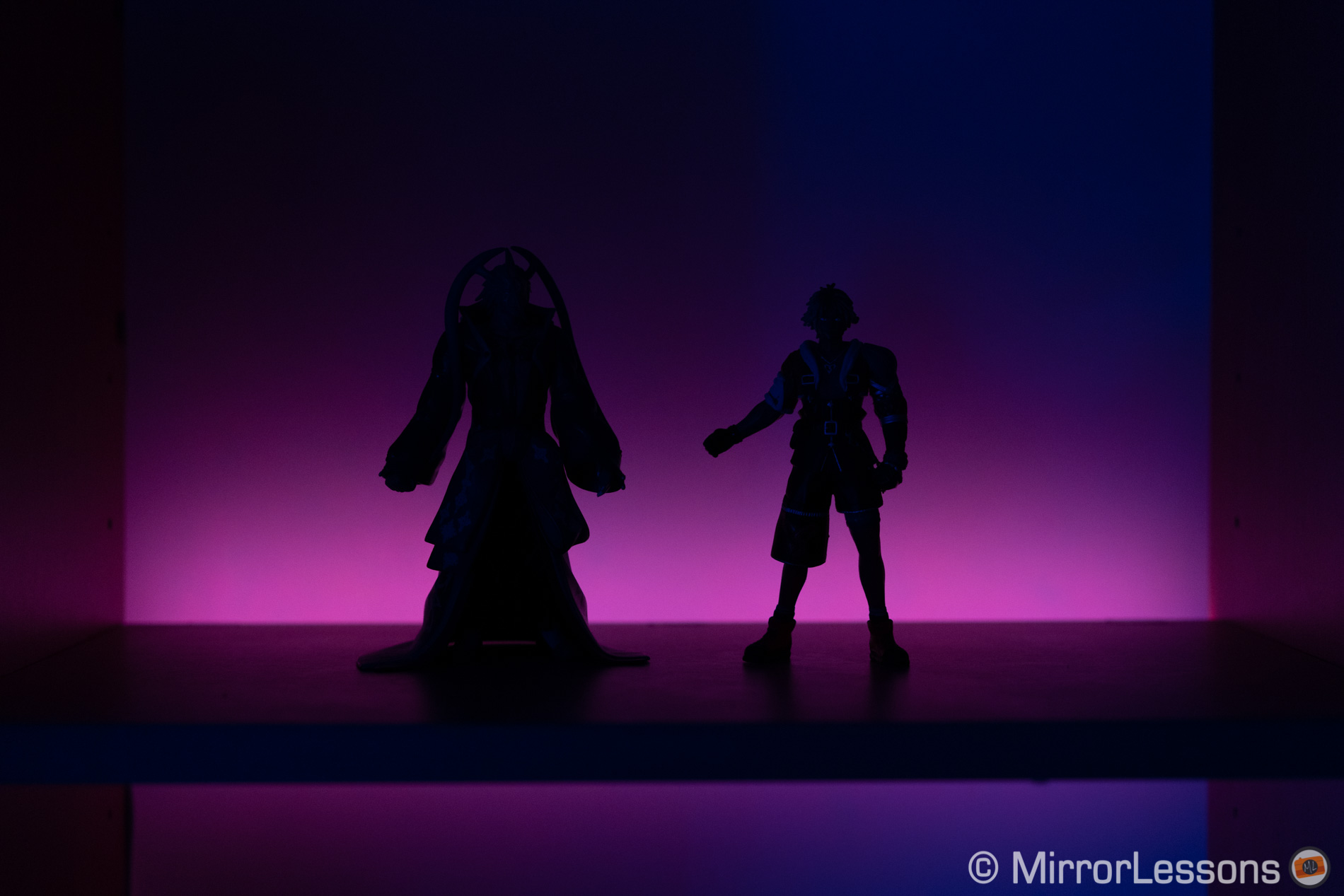 Silhueta de duas figuras de ação, com luz LED roxa ao fundo. Sem bandas
