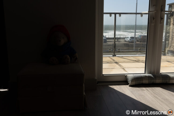 Stuffed toy in a living room with large window and view on of the sea on the outside