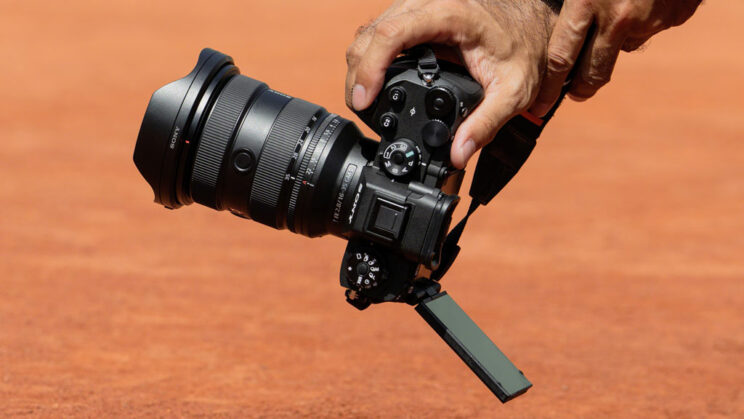 Photographer's hand holding the A9 III in vertical orientation with LCD titled up.